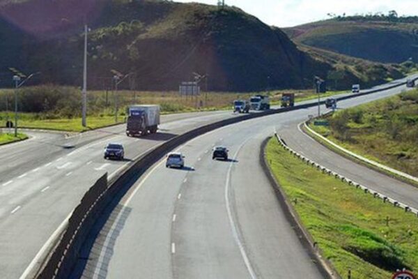 Rodovia com veículos em movimento e paisagem verde ao fundo.