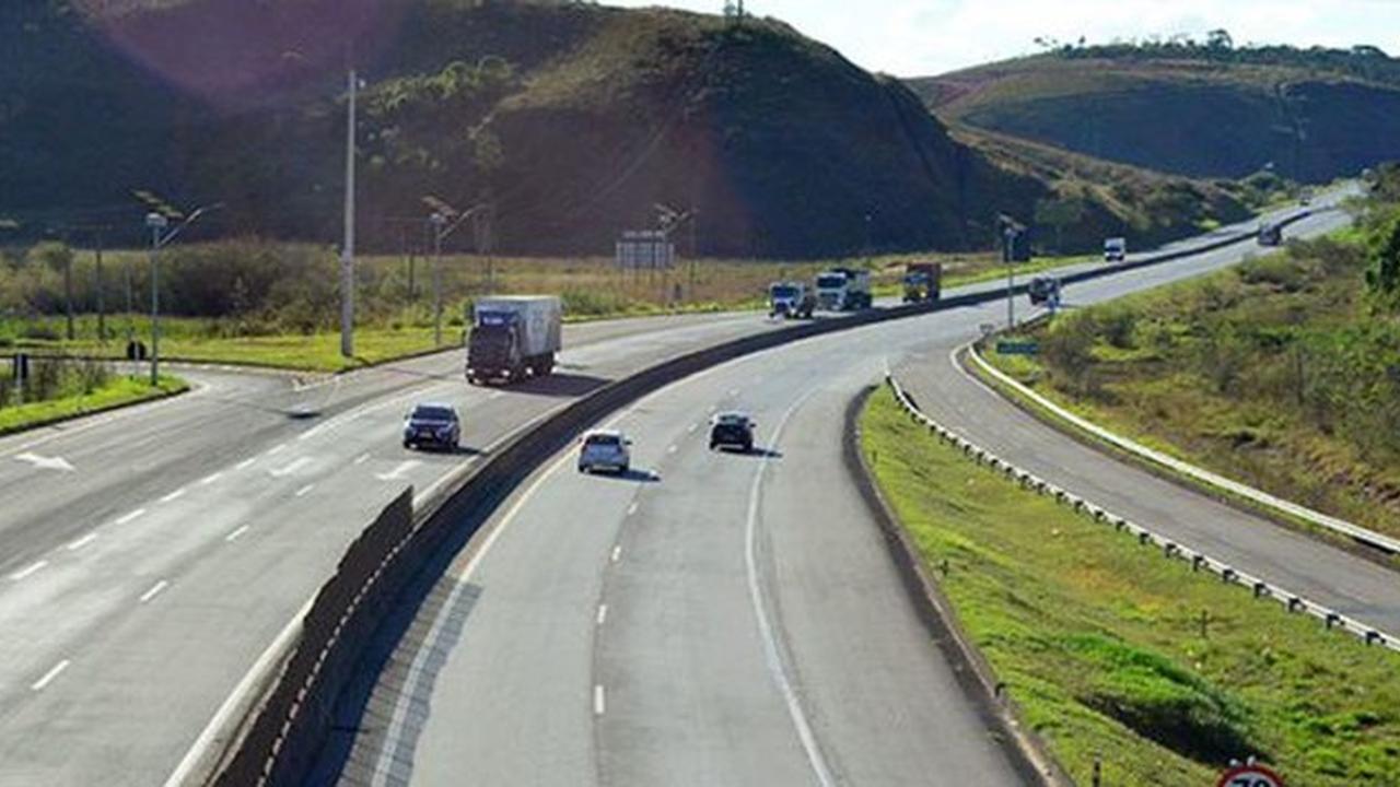 Rodovia com veículos em movimento e paisagem verde ao fundo.