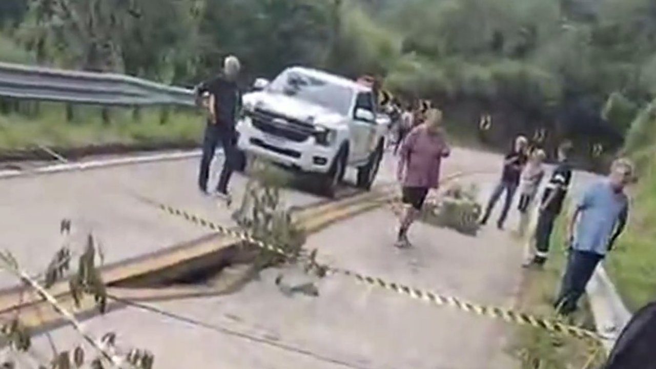 Rodovia interditada após parte da pista ceder, com carro parado e pessoas ao redor.