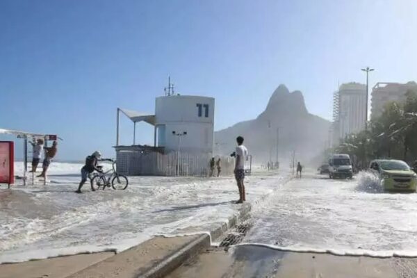 Rua alagada no Rio de Janeiro devido à ressaca marítima, com carros e pessoas afetadas.
