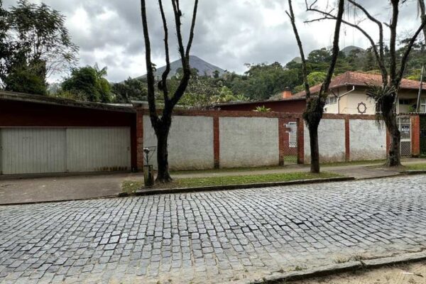 Rua de paralelepípedos com casas e árvores em dia nublado, com destaque para a mudança no trânsito.