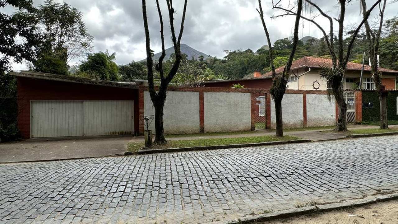 Rua de paralelepípedos com casas e árvores em dia nublado, com destaque para a mudança no trânsito.