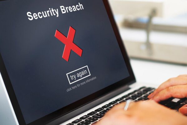 Tela de laptop com mensagem de 'Security Breach' e um 'X' vermelho, simbolizando tentativa de fraude.
