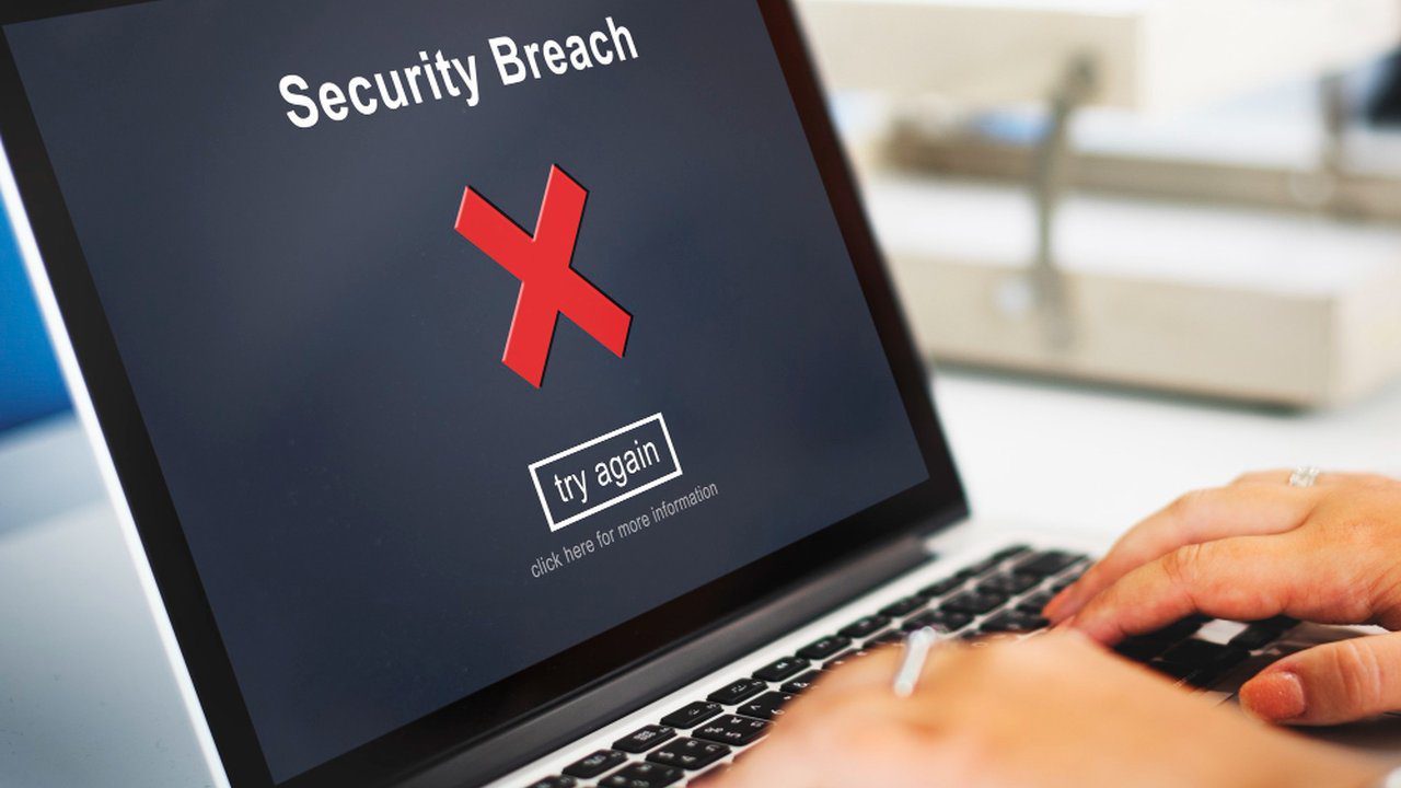 Tela de laptop com mensagem de 'Security Breach' e um 'X' vermelho, simbolizando tentativa de fraude.