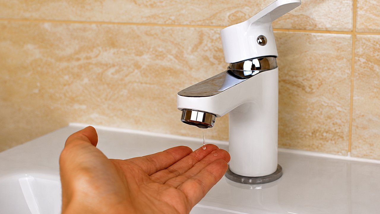Torneira com água pingando e mão para coletar, simbolizando preocupações com o abastecimento.