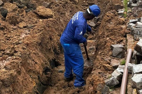 Trabalhador em obra cavando vala para instalação de tubulação de água.