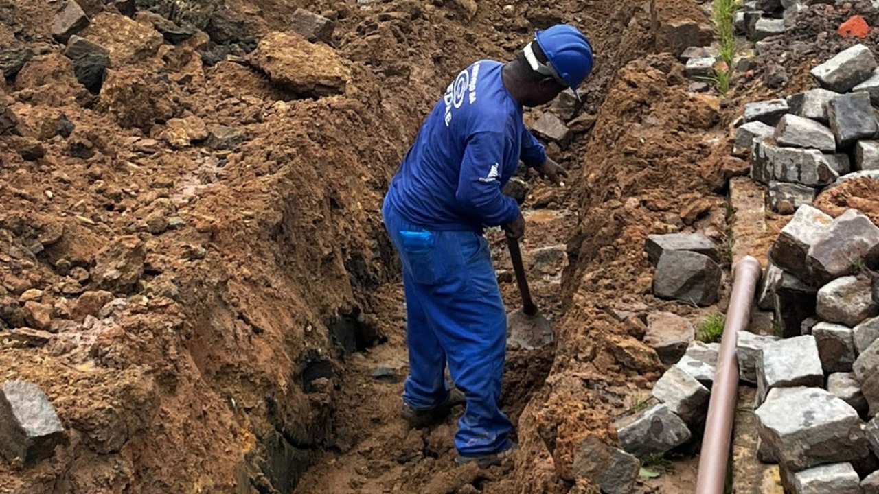 Trabalhador em obra cavando vala para instalação de tubulação de água.