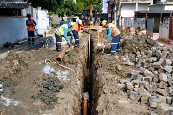 Trabalhadores consertando encanamento em via pública, com ferramentas e materiais.