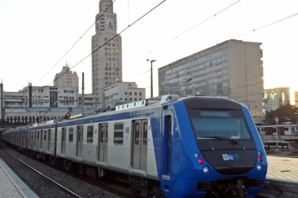 Trem azul e branco em estação no Rio de Janeiro, com prédios ao fundo.