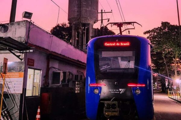 Trem da Supervia na estação Central do Brasil, com letreiro luminoso e céu rosado ao fundo.