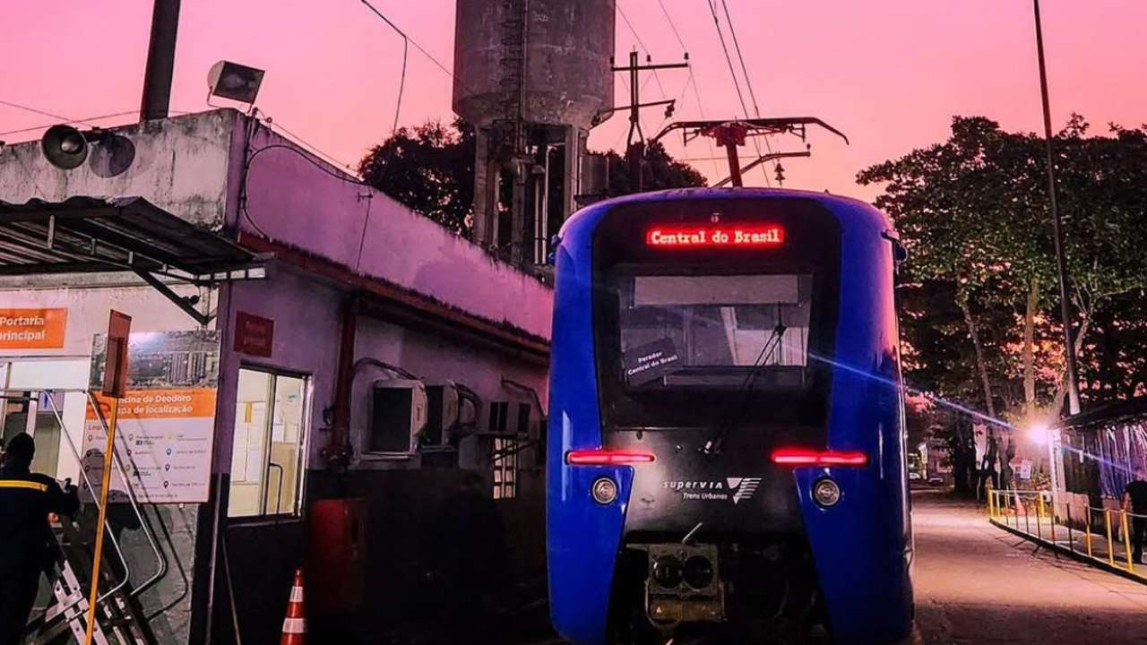 Trem da Supervia na estação Central do Brasil, com letreiro luminoso e céu rosado ao fundo.