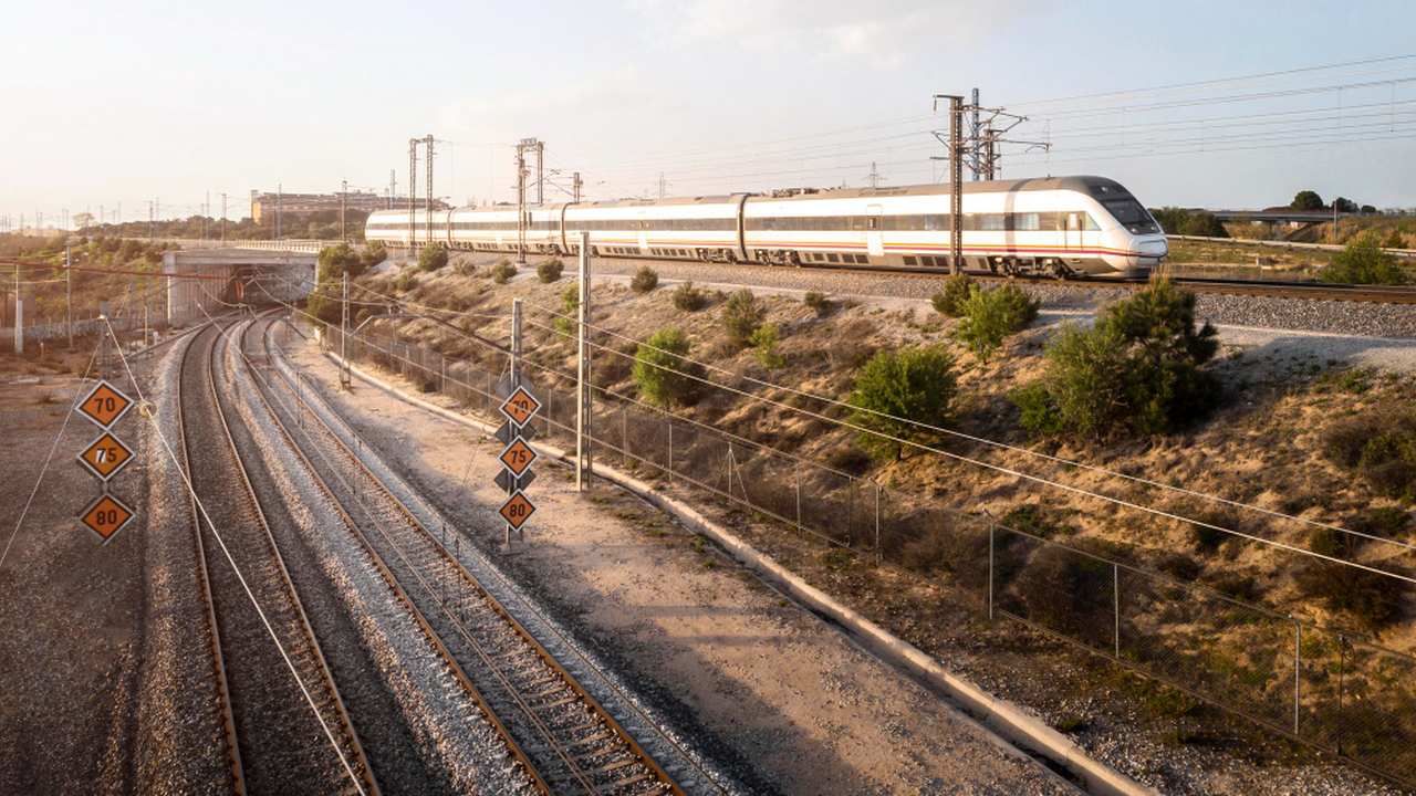 Trem em alta velocidade em trilhos ferroviários. Sinalização de velocidade visível.