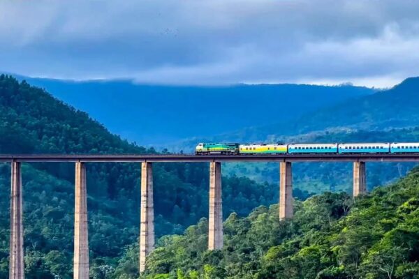 Trem percorrendo uma ponte em meio a montanhas arborizadas.