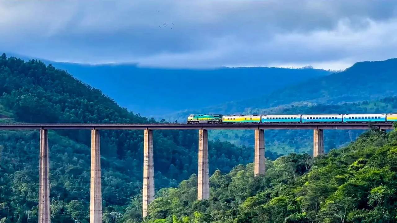 Trem percorrendo uma ponte em meio a montanhas arborizadas.