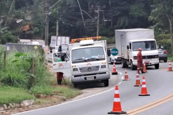 Veículos de trabalho em rodovia com cones laranjas e funcionários, sinalizando obras na pista.