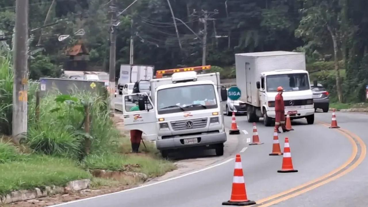 Veículos de trabalho em rodovia com cones laranjas e funcionários, sinalizando obras na pista.