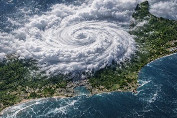 Visão aérea de um ciclone se aproximando de uma ilha com vegetação exuberante e mar azul.