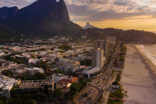 Vista aérea da orla e edifícios no Rio de Janeiro, com montanhas ao fundo.