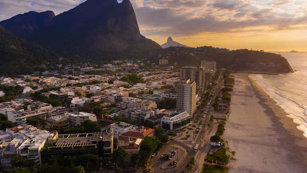 Vista aérea da orla e edifícios no Rio de Janeiro, com montanhas ao fundo.