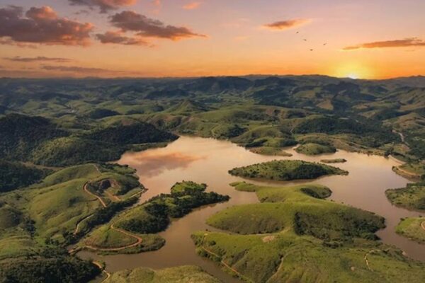 Vista aérea da paisagem exuberante com lago e montanhas ao pôr do sol, promessa de desenvolvimento turístico.