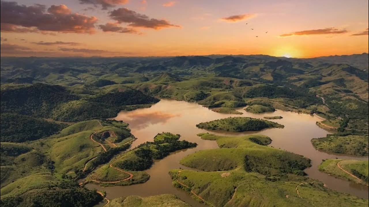 Vista aérea da paisagem exuberante com lago e montanhas ao pôr do sol, promessa de desenvolvimento turístico.