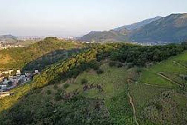 Vista aérea da paisagem montanhosa com áreas verdes e construção urbana ao fundo, em Campo Grande, Rio de Janeiro.