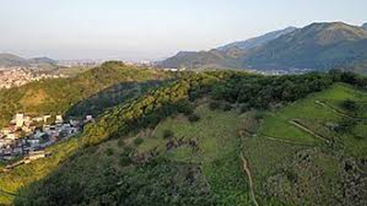 Vista aérea da paisagem montanhosa com áreas verdes e construção urbana ao fundo, em Campo Grande, Rio de Janeiro.