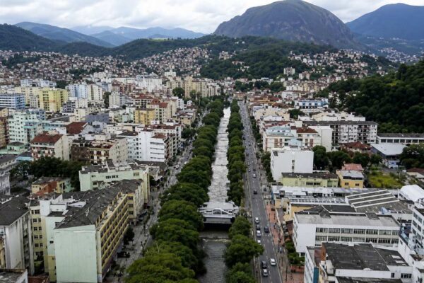 Vista aérea de Nova Friburgo, com prédios, rio e montanhas ao fundo.