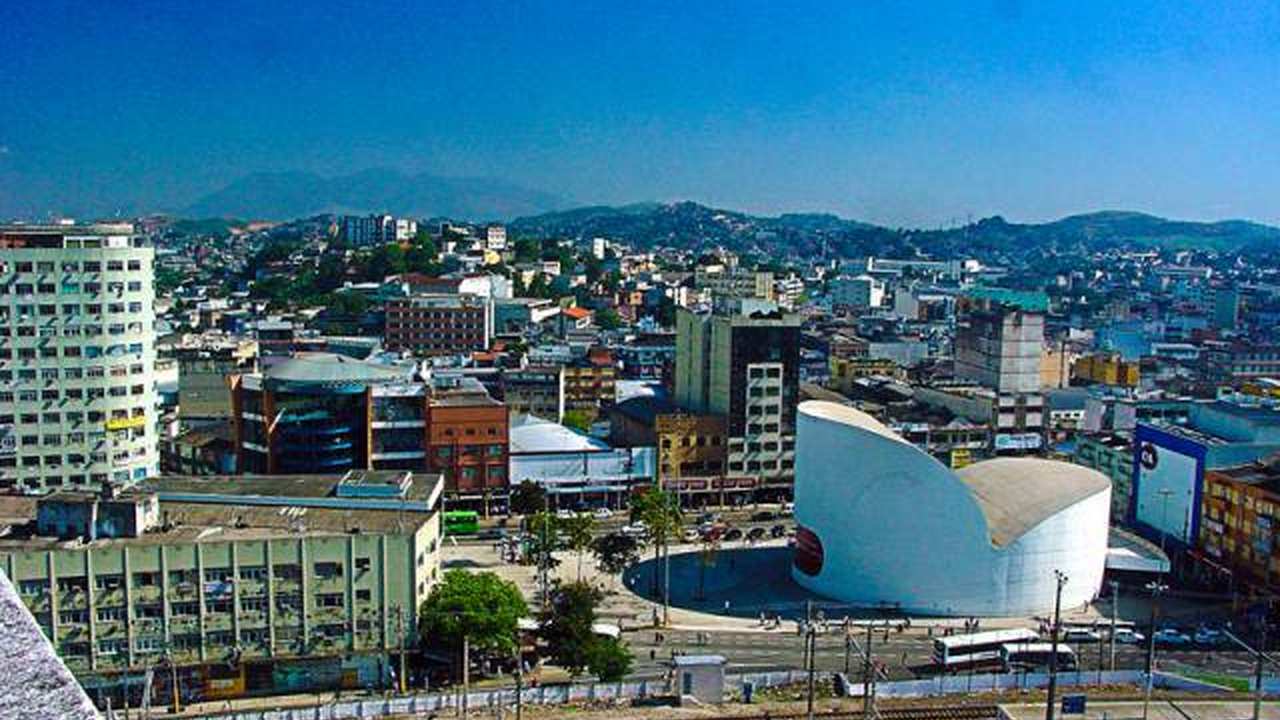 Vista panorâmica da cidade, com prédios e céu azul, possivelmente no Rio de Janeiro.