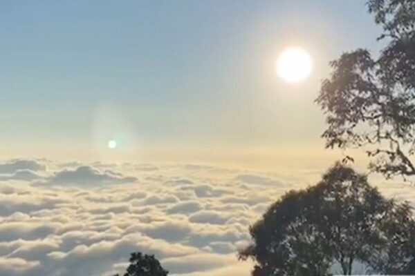Vista panorâmica do Pico do Caledônia com nuvens e dois sóis brilhantes, um fenômeno natural.