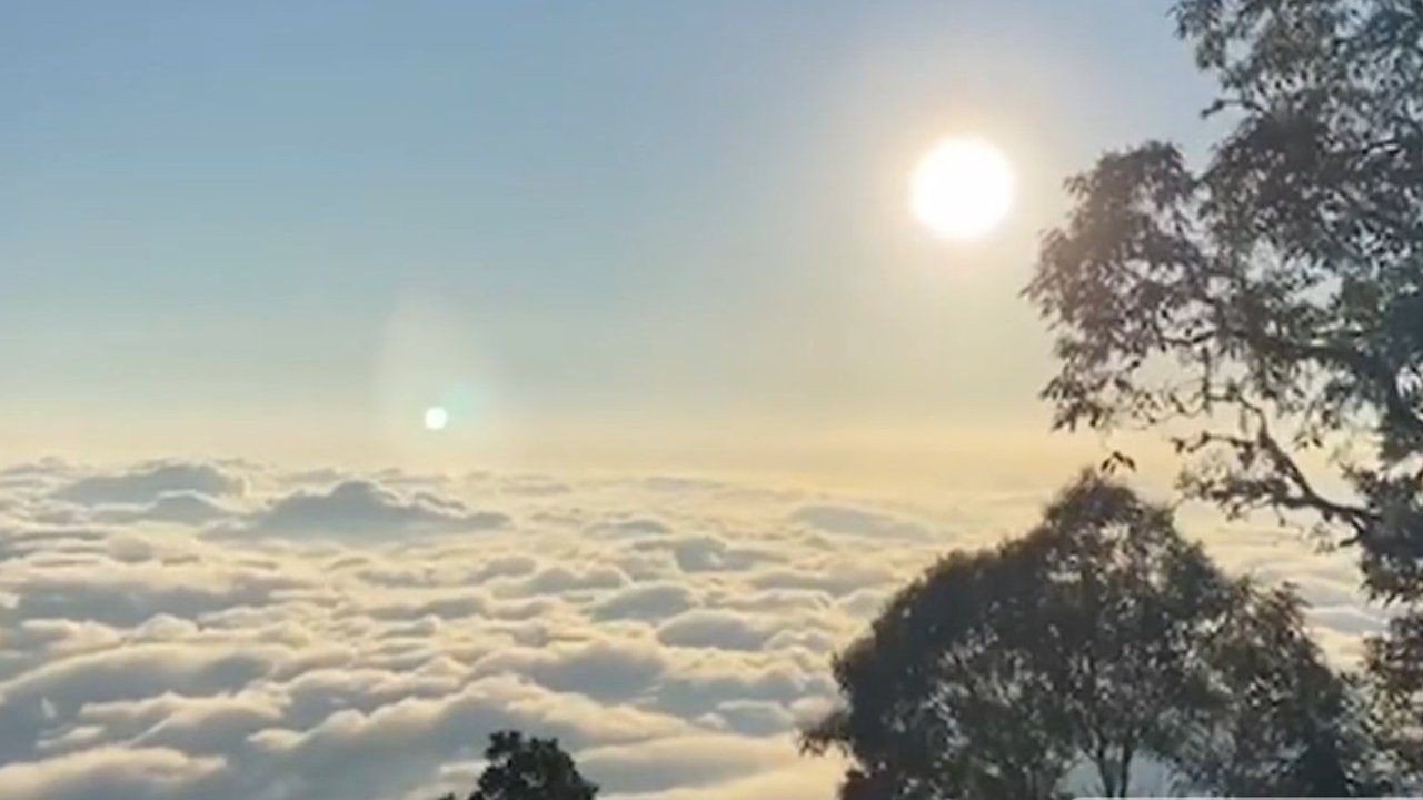 Vista panorâmica do Pico do Caledônia com nuvens e dois sóis brilhantes, um fenômeno natural.