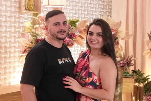 Samara e Robson posam juntos diante de uma decoração floral.
