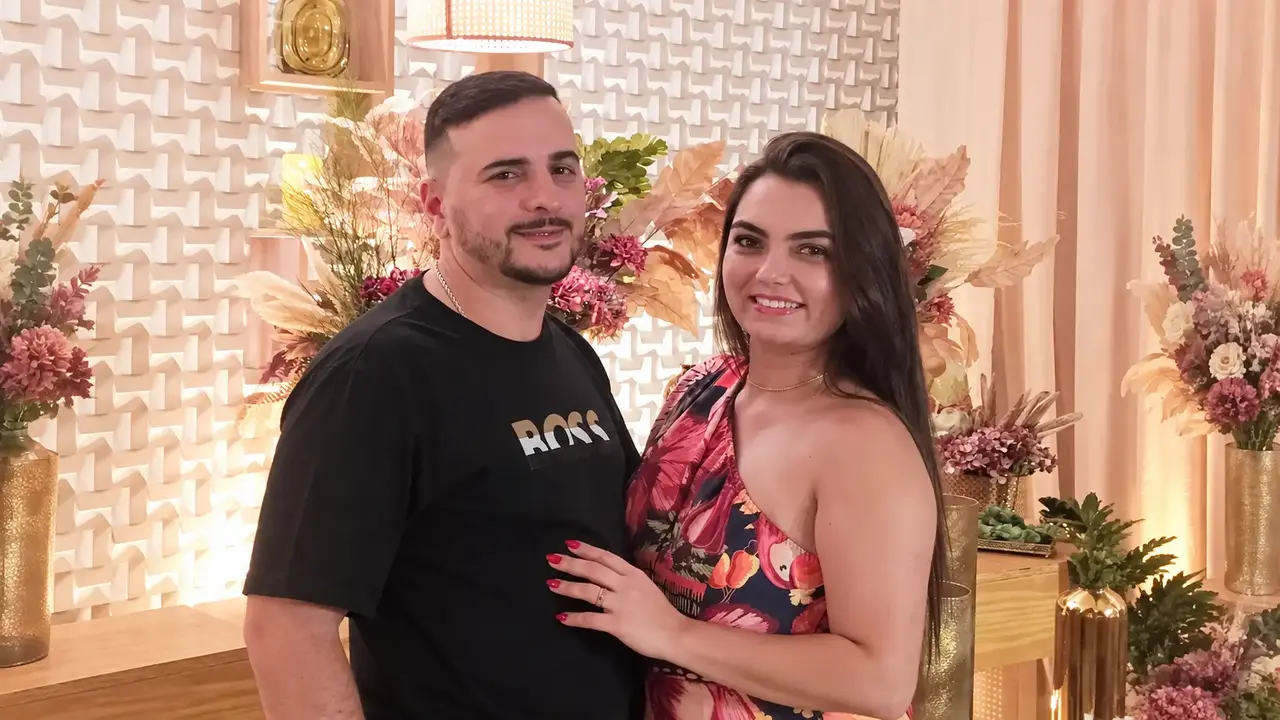 Samara e Robson posam juntos diante de uma decoração floral.