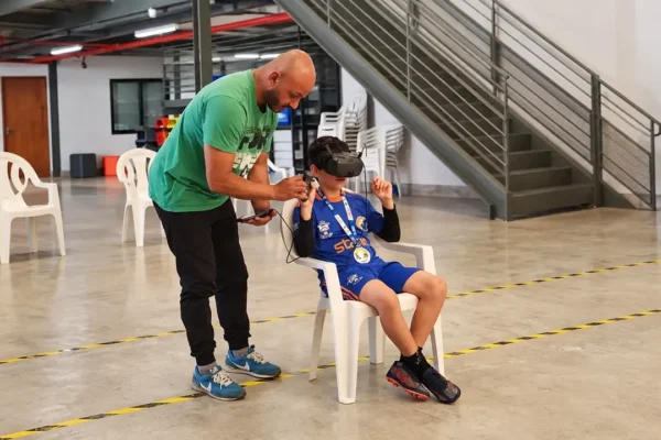 Adulto auxilia criança sentada a experimentar equipamento com visor durante atividade no Sesc Nova Friburgo