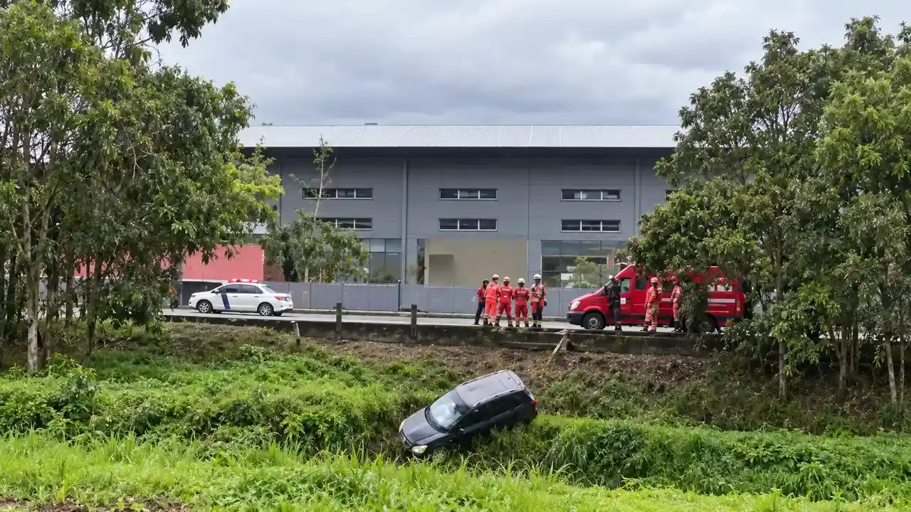 Carro preto em área de vegetação às margens do Rio Bengalas, com equipes de emergência próximas à pista