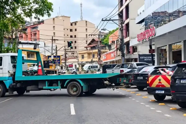 Caminhão-guincho com plataforma vazia no Paissandu, próximo a veículos estacionados e a uma viatura de trânsito.