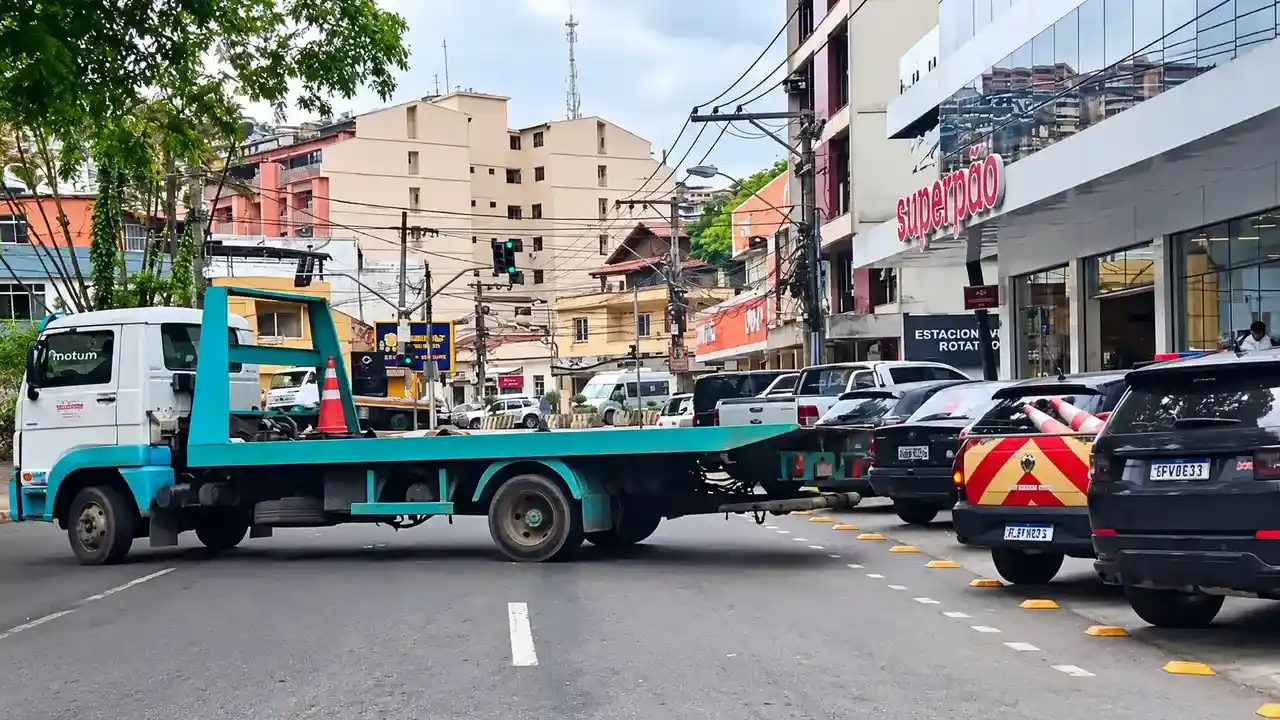 Caminhão-guincho com plataforma vazia no Paissandu, próximo a veículos estacionados e a uma viatura de trânsito.