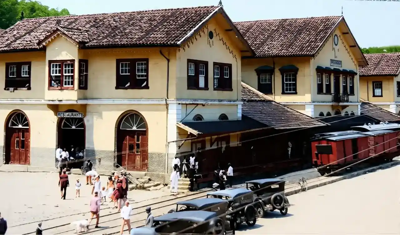 Vagões de trem junto a um prédio ferroviário, com pedestres e carros antigos em Nova Friburgo.