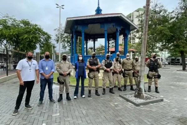 Grupo de pessoas, incluindo agentes uniformizados, posa diante de um coreto azul em uma praça.