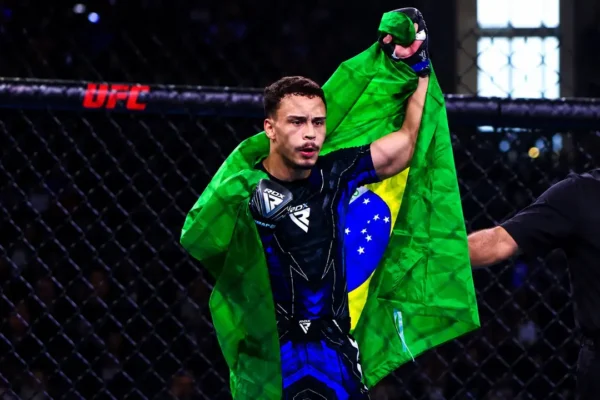 Davi Schuenck entra na arena com os braços abertos e a bandeira do Brasil nas costas.