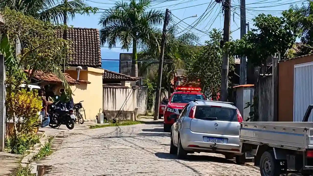 Rua residencial com viatura vermelha de resgate, veículos estacionados, moradores e postes com fiação aérea.