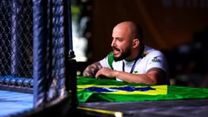 O treinador Filipe Grativol acompanha a competição ao lado da arena com uma bandeira do Brasil à sua frente.