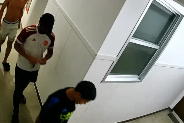 Três pessoas aparecem em um corredor, em imagem captada por câmera de segurança.