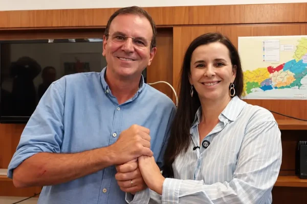 Eduardo Paes, à esquerda, e Jane Reis, à direita, sorrindo com as mãos unidas.
