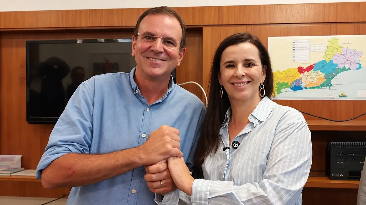 Eduardo Paes, à esquerda, e Jane Reis, à direita, sorrindo com as mãos unidas.