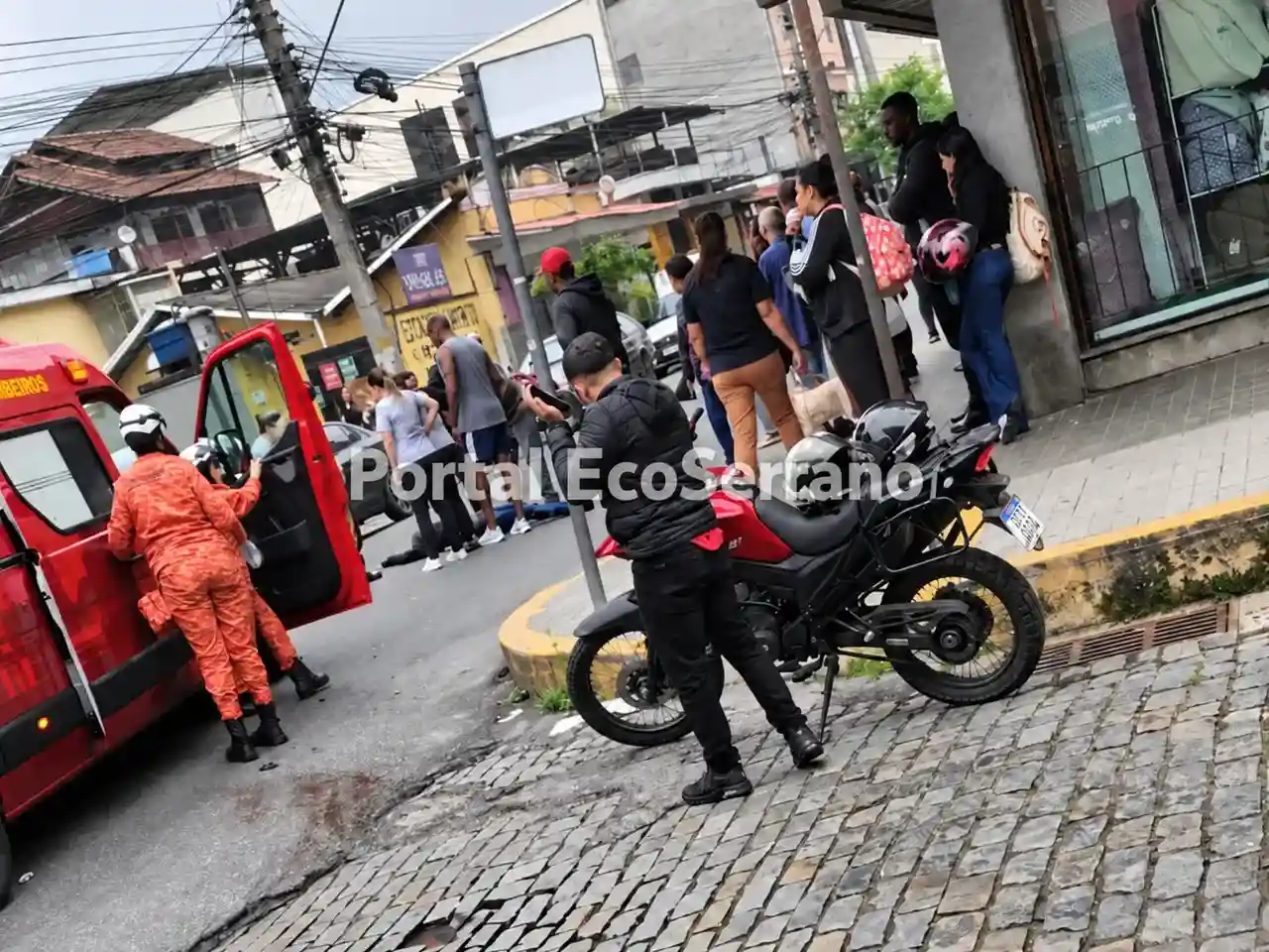 Bombeiro ao lado de veículo de resgate, com motocicleta e pessoas nas proximidades.