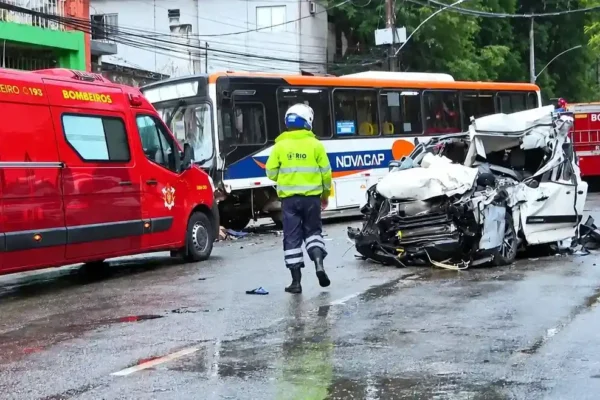 Carro branco severamente danificado ao lado de ônibus e viaturas dos bombeiros na Rua São Luiz Gonzaga.