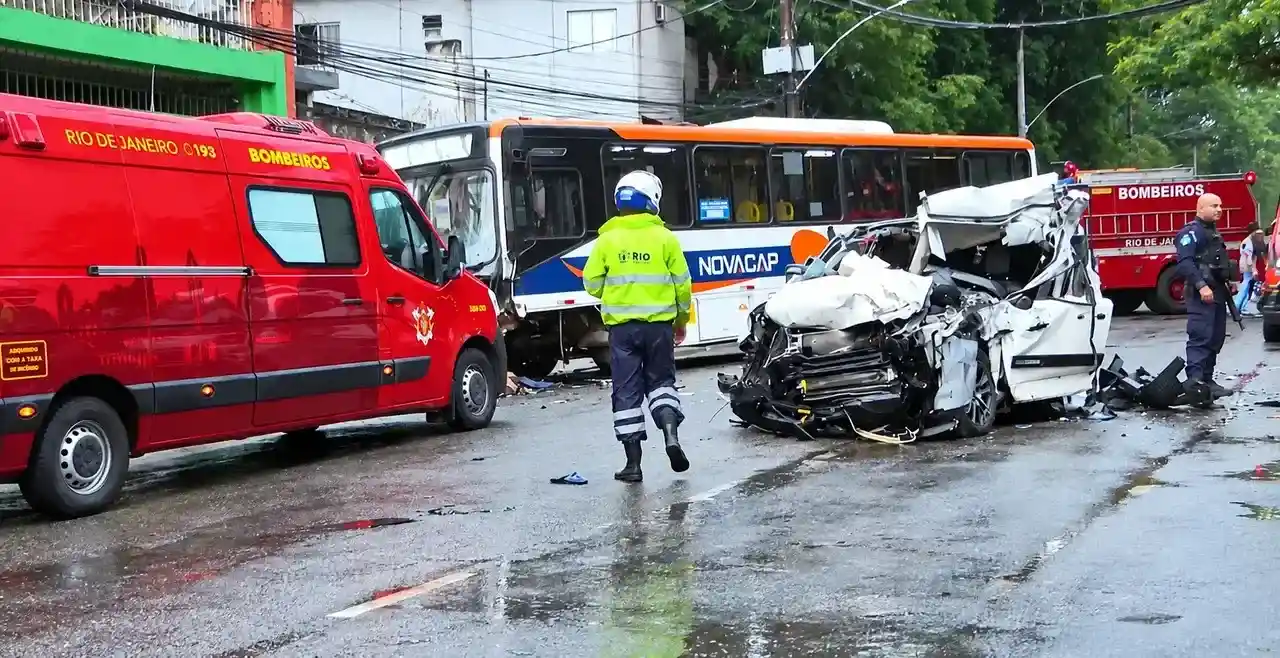 Carro branco severamente danificado ao lado de ônibus e viaturas dos bombeiros na Rua São Luiz Gonzaga.