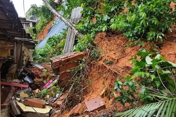 Encosta com terra exposta, vegetação caída e escombros ao lado de uma residência.