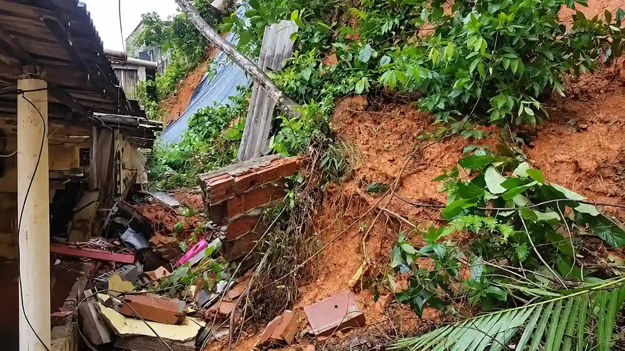 Encosta com terra exposta, vegetação caída e escombros ao lado de uma residência.